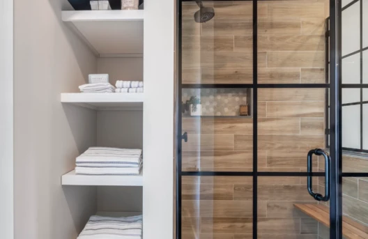 A modern bathroom shower with glass door and neatly stacked towels.