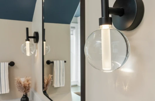 Modern bathroom with a round mirror and wall-mounted light.