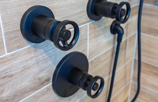 Black modern shower fixtures mounted on a beige tiled wall.