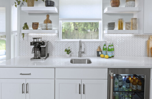 Bright Kitchen Remodel With White Shaker Cabinets, Navy Blue Island, Herringbone Tile Backsplash, Stainless Steel Range Hood, Under-Counter Wine Fridge and Open Shelving
