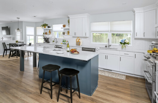 Bright Kitchen Remodel With White Shaker Cabinets, Navy Blue Island, Herringbone Tile Backsplash, Stainless Steel Range Hood, Under-Counter Wine Fridge and Open Shelving