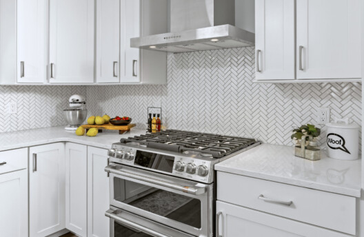 Bright Kitchen Remodel With White Shaker Cabinets, Navy Blue Island, Herringbone Tile Backsplash, Stainless Steel Range Hood, Under-Counter Wine Fridge and Open Shelving