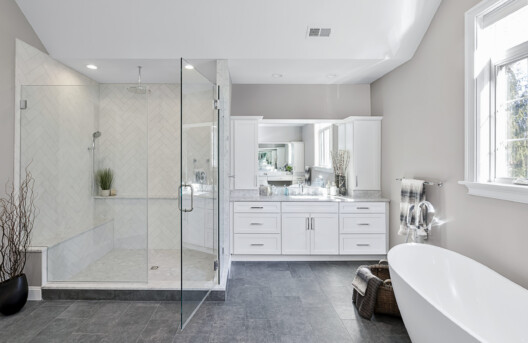 Primary Bathroom Remodel in Lower Gwynned Township, Ambler, PA. Features 4" x 12" Honed White Carrara Marble In The Shower With Full Back-Wall Shelf, Freestanding Tub, Dual Vanities with Marble Tops, Glass Shower Enclosure, and Custom White Cabinetry and Built-In Bench