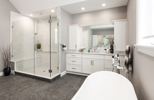Primary Bathroom Remodel in Lower Gwynned Township, Ambler, PA. Features 4" x 12" Honed White Carrara Marble In The Shower With Full Back-Wall Shelf, Freestanding Tub, Dual Vanities with Marble Tops, Glass Shower Enclosure, and Custom White Cabinetry and Built-In Bench