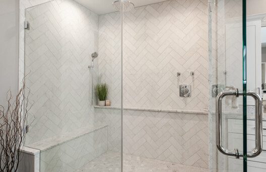 Primary Bathroom Remodel in Lower Gwynned Township, Ambler, PA. Features 4" x 12" Honed White Carrara Marble In The Shower With Full Back-Wall Shelf, Freestanding Tub, Dual Vanities with Marble Tops, Glass Shower Enclosure, and Custom White Cabinetry and Built-In Bench