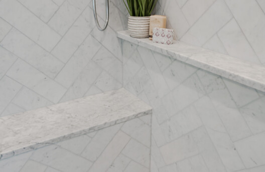 Primary Bathroom Remodel in Lower Gwynned Township, Ambler, PA. Features 4" x 12" Honed White Carrara Marble In The Shower With Full Back-Wall Shelf, Freestanding Tub, Dual Vanities with Marble Tops, Glass Shower Enclosure, and Custom White Cabinetry and Built-In Bench